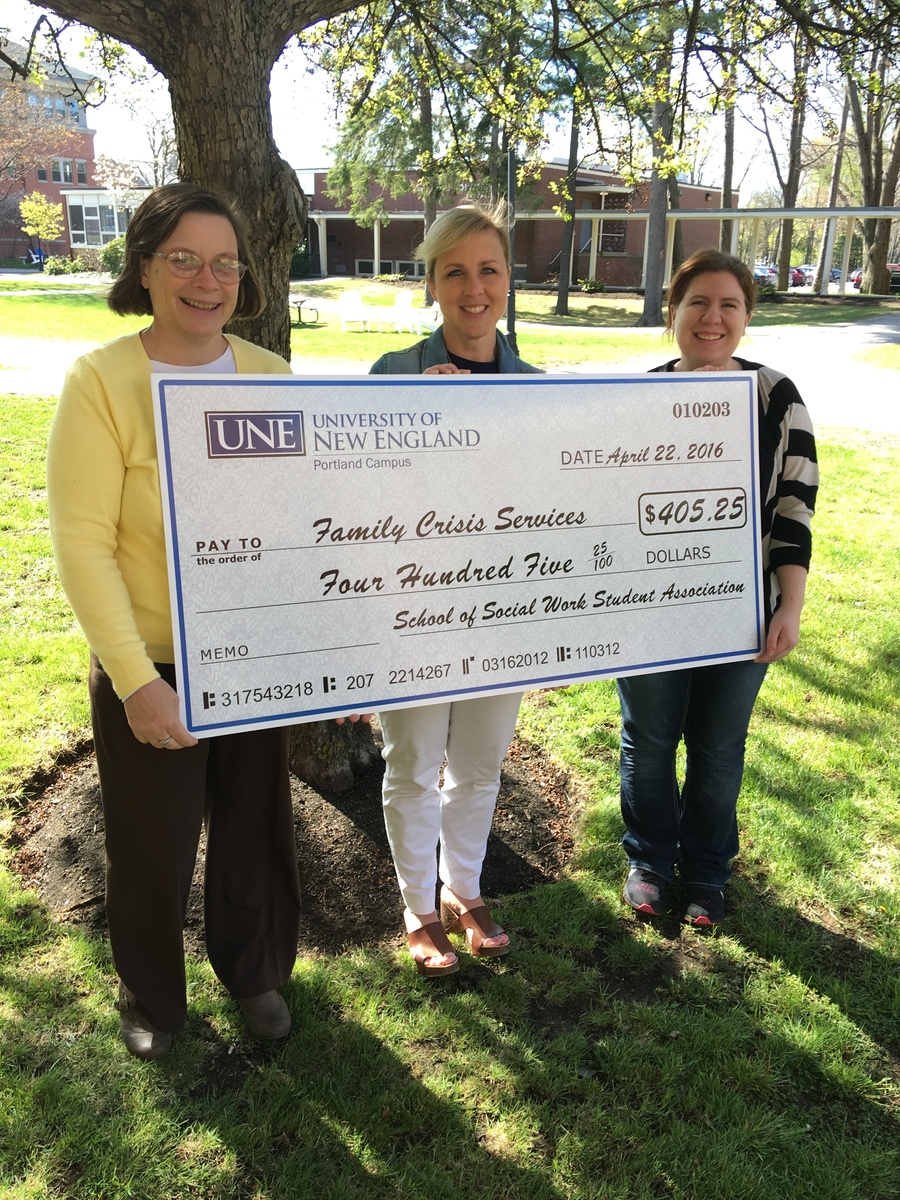 Three students from U N E's school of social work present a check to a local social work agency